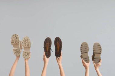 Gri arkaplanda farklı çizmeler tutan kadın eller.