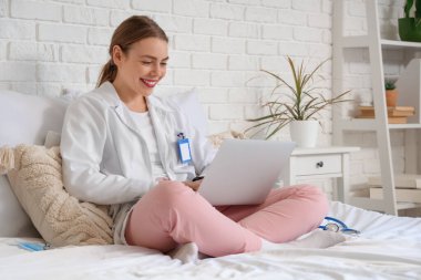 Genç bayan tıp öğrencisi evdeki yatağında modern laptop kullanıyor.