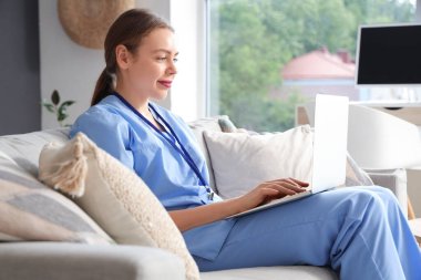 Genç bayan tıp öğrencisi evdeki koltukta modern dizüstü bilgisayar kullanıyor.