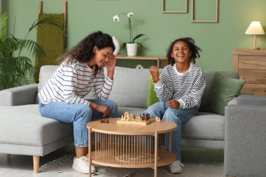Genç ve güzel mutlu Afro-Amerikan anne ve kızı evdeki kanepede satranç oynuyorlar.