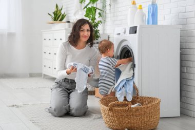 Genç anne ve tatlı bebeği çamaşır odasında çamaşır makinesine koyuyorlar.