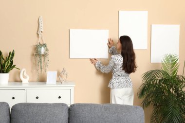 Evdeki bej duvara boş tuval asan genç bir kadın.