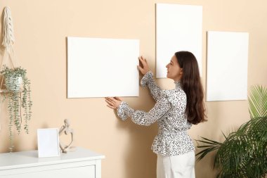 Evdeki bej duvara boş tuval asan genç bir kadın.
