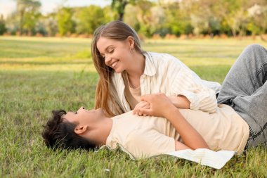 Güzel, genç ve mutlu bir çift yaz parkında çimlerin üzerinde yatıyor.
