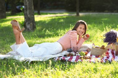 Piknikte şeftaliyle ekose üzerinde uzanan güzel genç bir kadın.