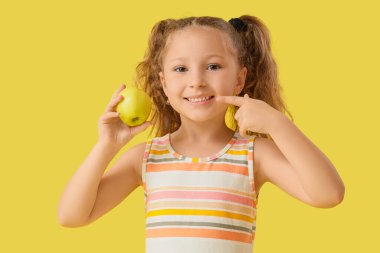 Sarı arka planda yeşil elmayı gösteren sevimli küçük kız.