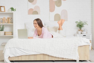 Evde dizüstü bilgisayar kullanan genç bir kadın.