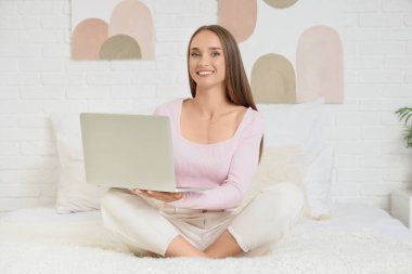 Yatak odasında dizüstü bilgisayar kullanan genç kadın.