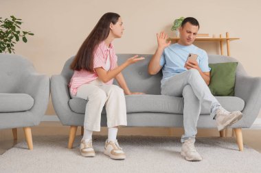 Evde cep telefonuyla kocasıyla kavga eden genç bir kadın.