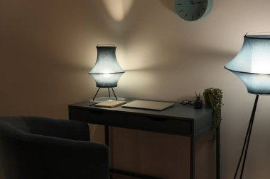 Geceleri ofiste gri duvarın yanında lamba ve modern dizüstü bilgisayarı olan şık bir iş yeri.