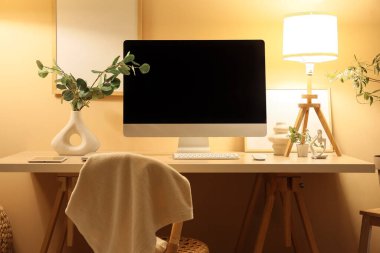 Modern bilgisayarlı şık bir iş yeri ve geceleri ofiste sarı duvarın yanında parlayan lambalar.