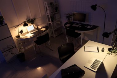 Masaları, bitkileri ve parlayan lambaları olan karanlık ofisin içinde.