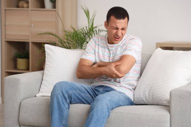 Genç adam evdeki kanepede dirseğinde ağrıdan muzdarip.