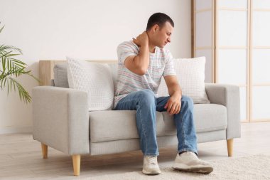 Evdeki kanepede boynundaki ağrıdan muzdarip genç adam.