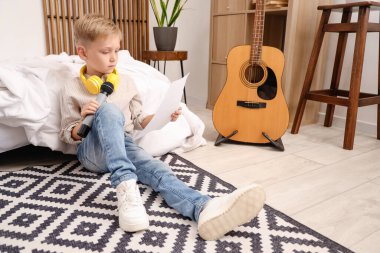 Kulaklıkları ve mikrofonuyla evde nota okuyan sevimli küçük bir çocuk.