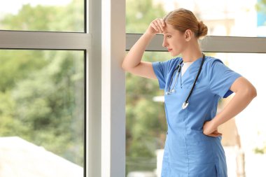 Kliniğin penceresinin yanında steteskobu olan yorgun kadın doktor.