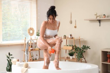 Güzel, genç, mutlu bir Afro-Amerikan kadın evde sünger ve sabun köpüğüyle banyo yapıyor.