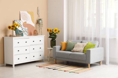 Koltuk, çekmeceler ve vazolarla dolu. Oturma odasının içinde güzel ayçiçekleri var.