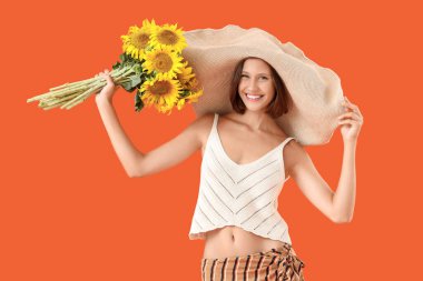 Hasır şapkalı, turuncu arka planda bir buket ayçiçeği olan güzel, genç ve mutlu bir kadın.