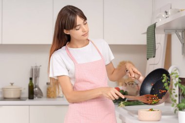 Genç ev hanımı mutfakta kızarmış sebzeleri kaseye koyuyor.