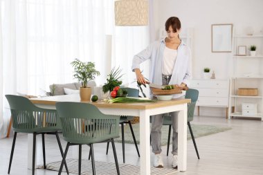 Genç bir kadın yemek odasındaki masaya salatalık koyuyor.