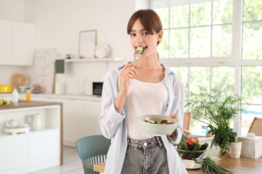 Genç bir kadın yemek odasında sebze salatası yiyor.