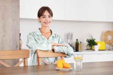 Genç bir kadın mutfakta sandalyeye yaslanıyor.