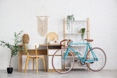 Çalışma odası, raf ünitesi ve bisiklet beyaz tuğla duvarın yanında.