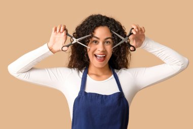 Bej arka planda makasıyla güzel, mutlu, Afro-Amerikalı bir kuaför.