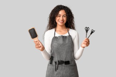 Gri arka planda fırça ve makasla güzel, mutlu, Afro-Amerikan kuaför.