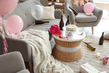 Şişeli doğum günü pastası ve dağınık oturma odasındaki masanın üstünde parti dekoru.