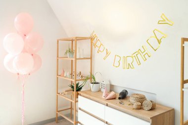 Doğum gününden sonra dağınık oturma odasının içinde raf ünitesi, çekmeceler ve parti dekoruyla