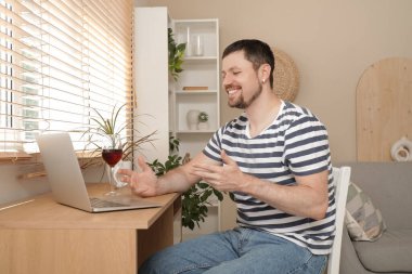 Masada dizüstü bilgisayarı olan yakışıklı bir adamın evde online randevusu var.