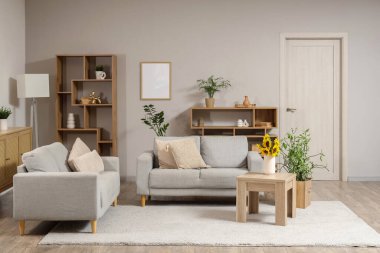 Ahşap sehpanın üzerinde gri kanepeler ve ayçiçekleri olan modern oturma odasının içinde.