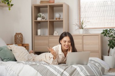 Bilgisayarlı genç Asyalı kadın yatak odasında online randevusu var.