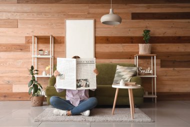 Gazetesi olan genç bir kadın evdeki kanepenin yanında oturuyor.