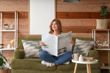 Evdeki rahat kanepede oturan gazeteli güzel genç bir kadın.