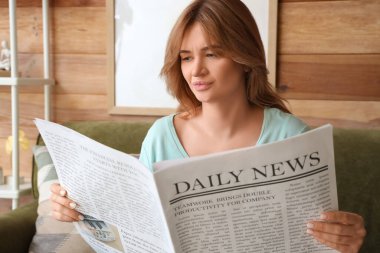 Evdeki rahat kanepede oturan gazeteli güzel genç bir kadın.