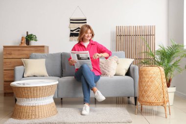 Evdeki kanepede gazete kontrol eden genç bir kadın.