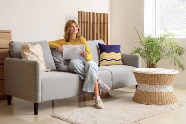 Evdeki kanepede gazete okuyan güzel bir genç bayan.