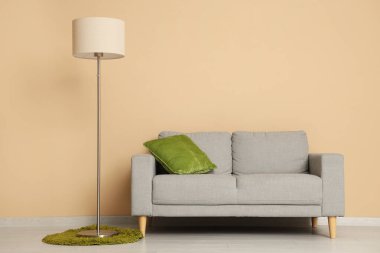 Oda, bej duvarın yanında rahat bir kanepe ve zemin lambası.