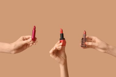 Kahverengi arka planda farklı ruj izleri olan kadın elleri.