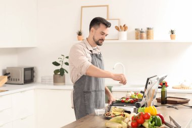 Genç adam lezzetli sebzelere tuz ekliyor mutfaktaki modern elektrikli ızgaraya şiş koyuyor.