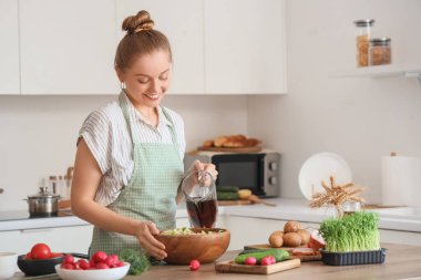 Genç bir kadın mutfakta okroshka 'ya kvass döküyor.