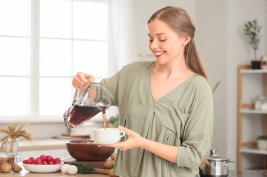 Genç bir kadın mutfakta okroshka 'ya kvass döküyor.