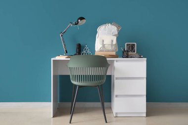 Mavi duvarın yanında lamba, saat ve okul çantası olan şık çocuk işyeri.