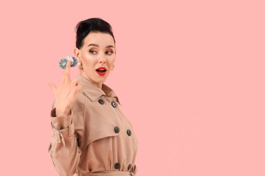 Pembe arka planda poker fişleri olan paltolu genç bir kadın.