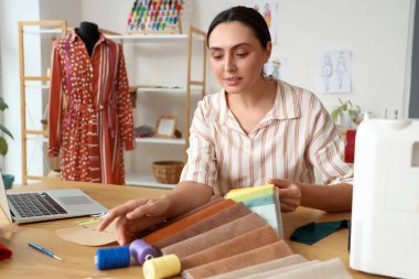 Atölyedeki masada kumaş örnekleriyle çalışan kadın terzi.