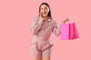 Pembe arka planda alışveriş torbaları olan şaşırmış genç bir kadın.