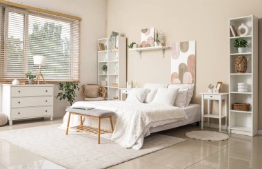 Yumuşak bank, raf üniteleri ve tabloları olan şık bir yatak odası.